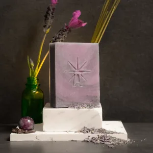 Styled scene featuring Black Altar lavender-hued Mystic Twilight soap on stacked white marble blocks, with dried lavender stems in a green glass bottle behind it and scattered lavender buds and an amethyst sphere in front.