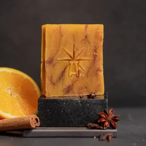 Black Altar Ritual Ember soap—warm amber bar on a dark stone pedestal, framed by a sliced orange, cinnamon stick, star anise, and cloves.