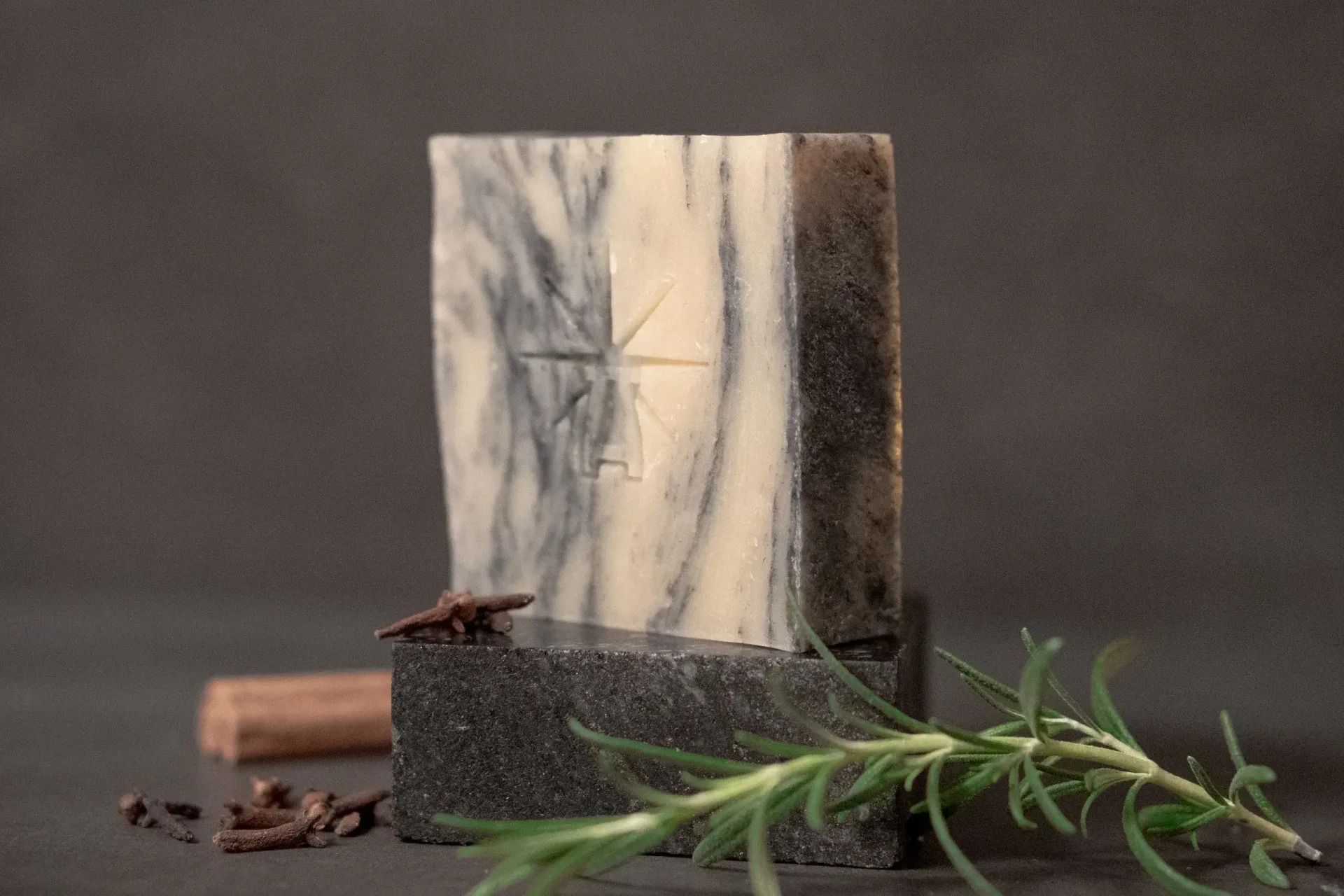 Black Altar Sacred Marble soap—cream and charcoal-swirled bar on dark stone, styled with fresh rosemary, cloves, and a cinnamon stick.