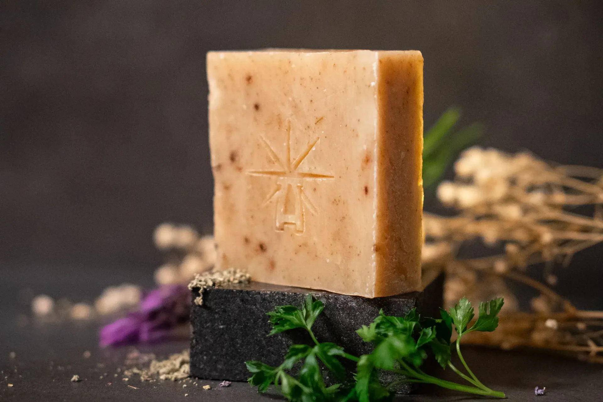 Black Altar Witch bloom soap—warm beige bar flecked with botanicals, star-altar logo embossed, styled on black stone with parsley, lavender, and dried sage.