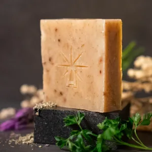 Black Altar Witch bloom soap—warm beige bar flecked with botanicals, star-altar logo embossed, styled on black stone with parsley, lavender, and dried sage.