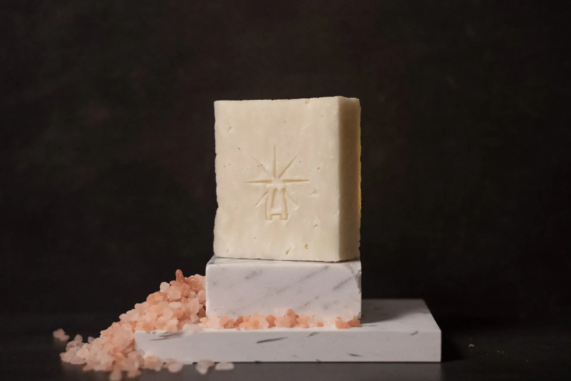 Black Altar Earth Salt soap—creamy off-white bar on stacked white marble blocks, pink Himalayan salt crystals spilling alongside.