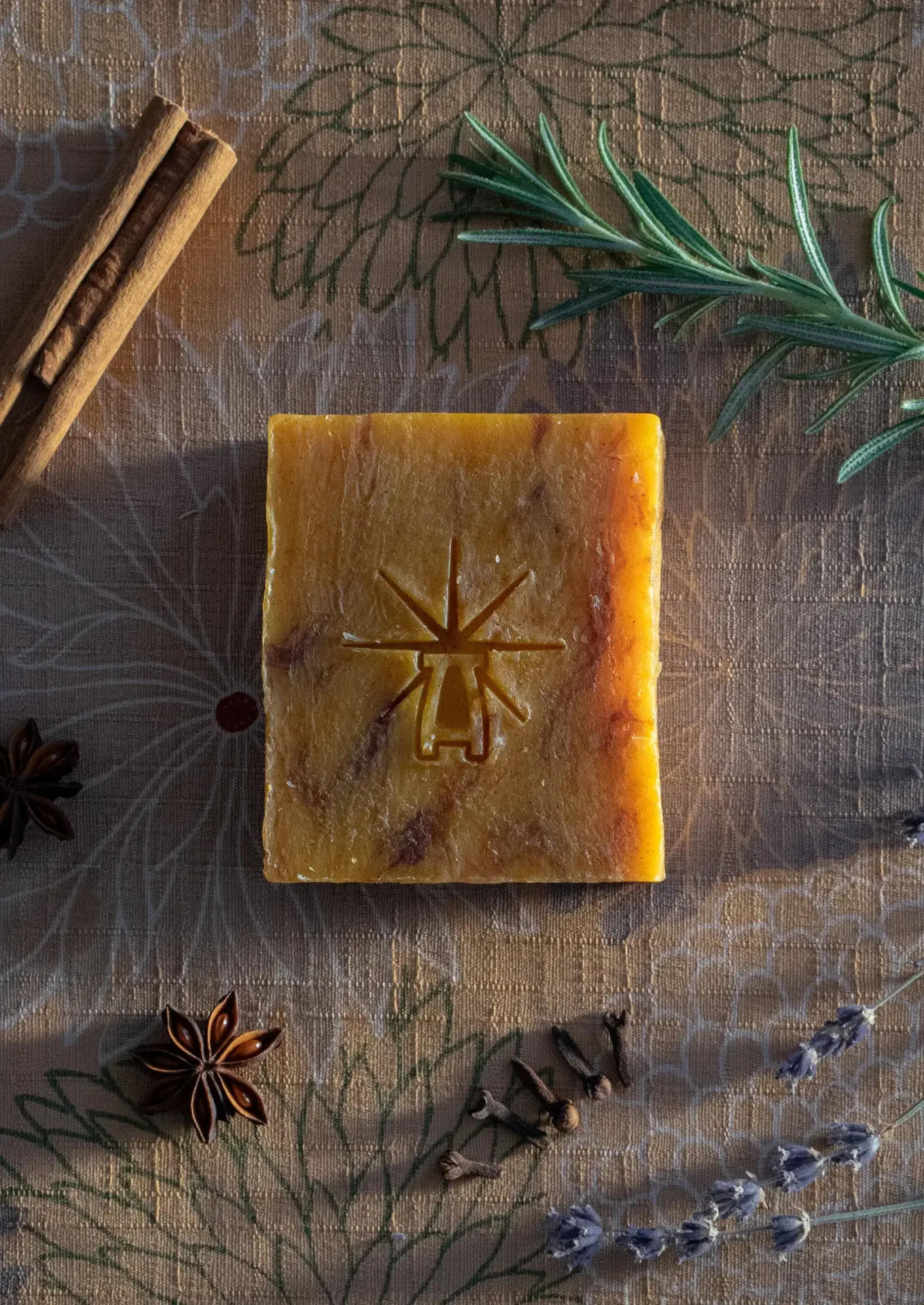 Flat-lay of Black Altar Ritual Ember soap on patterned cloth, framed by rosemary, cinnamon stick, star anise, cloves, and lavender sprig.
