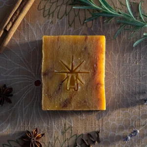 Flat-lay of Black Altar Ritual Ember soap on patterned cloth, framed by rosemary, cinnamon stick, star anise, cloves, and lavender sprig.