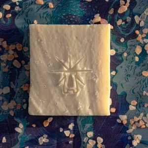 Flat-lay of Black Altar Earth Salt soap on ocean-blue fabric, scattered with coarse pink Himalayan salt crystals.