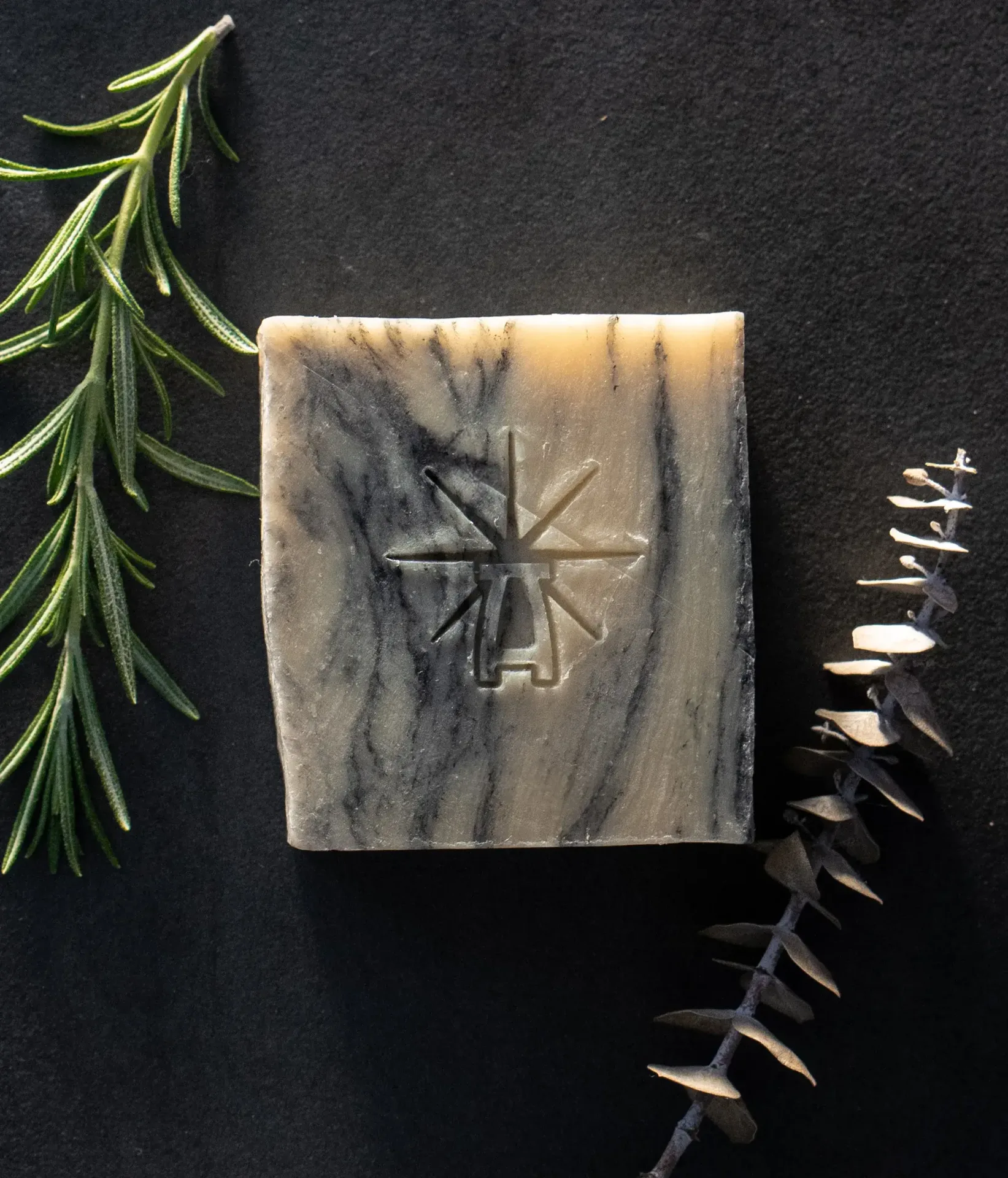 Black Altar Sacred Marble soap on dark backdrop, styled with fresh rosemary and a dried eucalyptus stem.