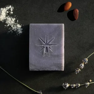 Black Altar Mystic Twilight soap on dark surface, accented by powdered clay, two shea butter nuts, and dried lavender stems.