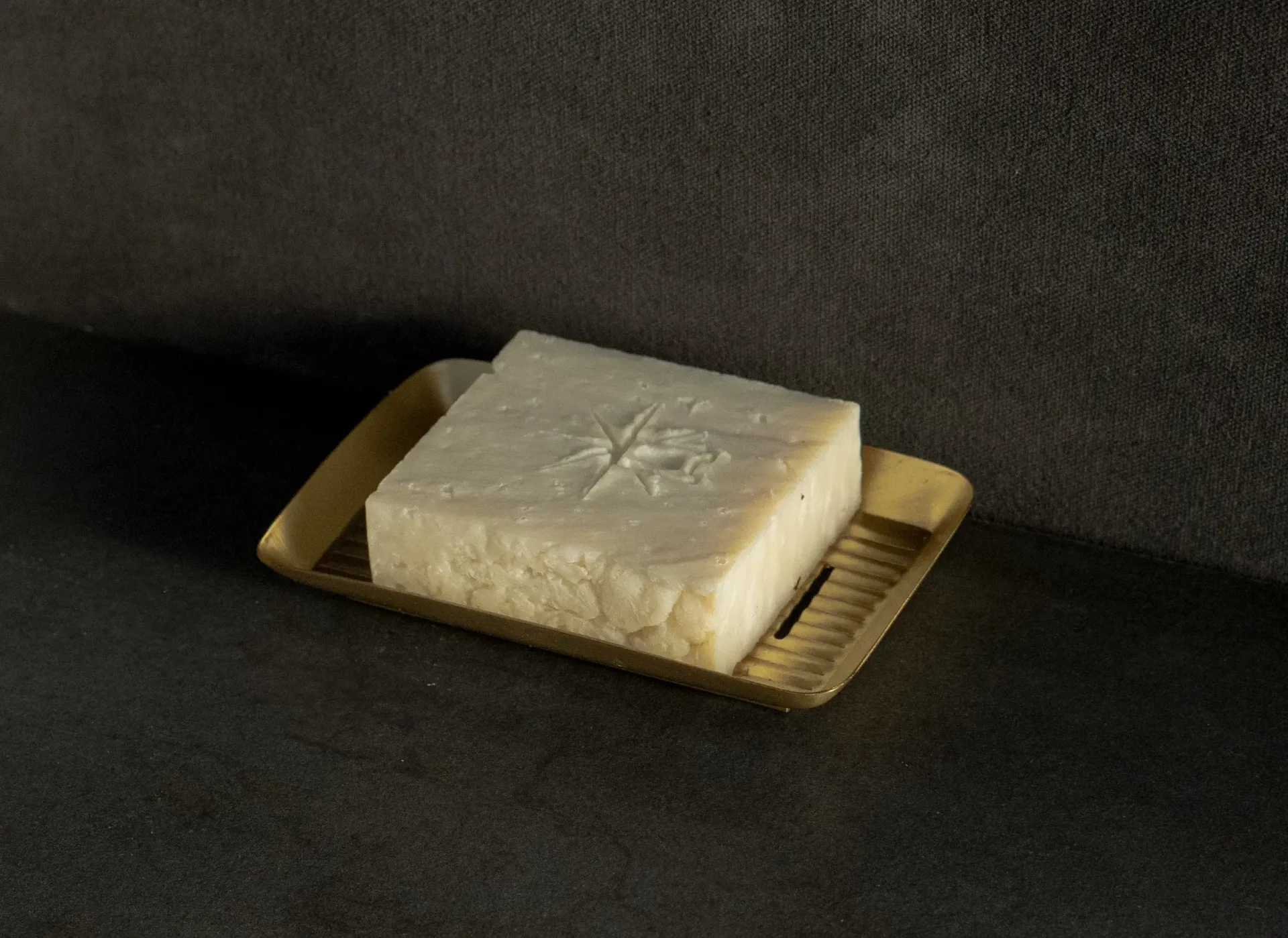Black Altar Earth Salt soap resting in a gold metal dish on a granite countertop.