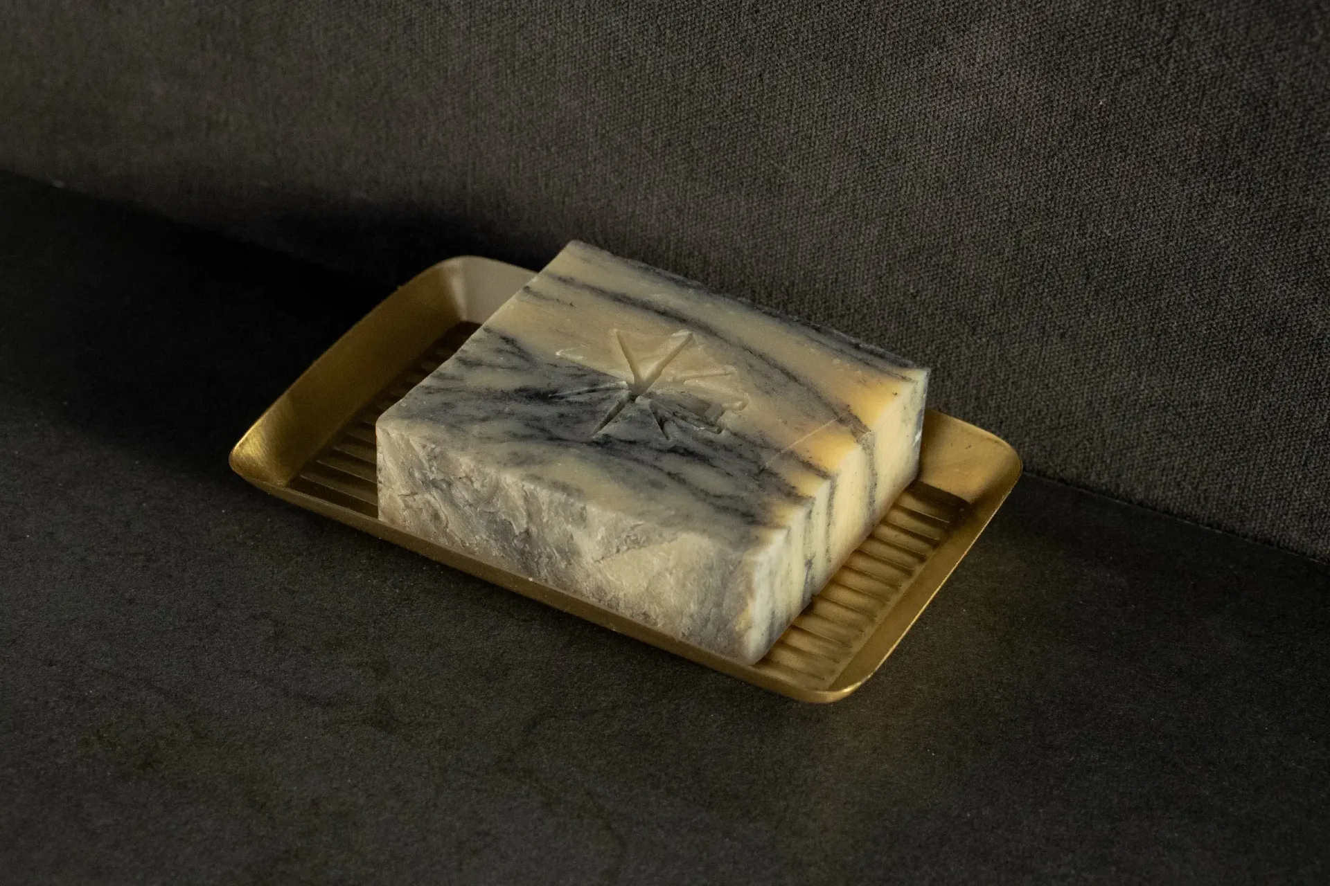 Black Altar Sacred Marble soap resting in a gold metal dish on a granite countertop.