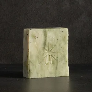 Studio shot of Black Altar Wild Conjuring soap—pale green bar with dark poppy specks and star-altar logo on dark backdrop.