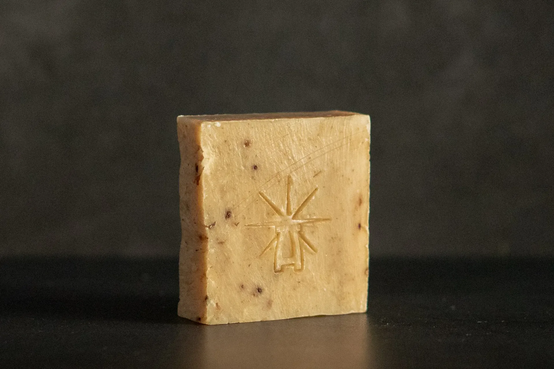 Studio shot of Black Altar Witch Bloom soap—beige botanical bar flecked with herbs, featuring the star-altar logo.