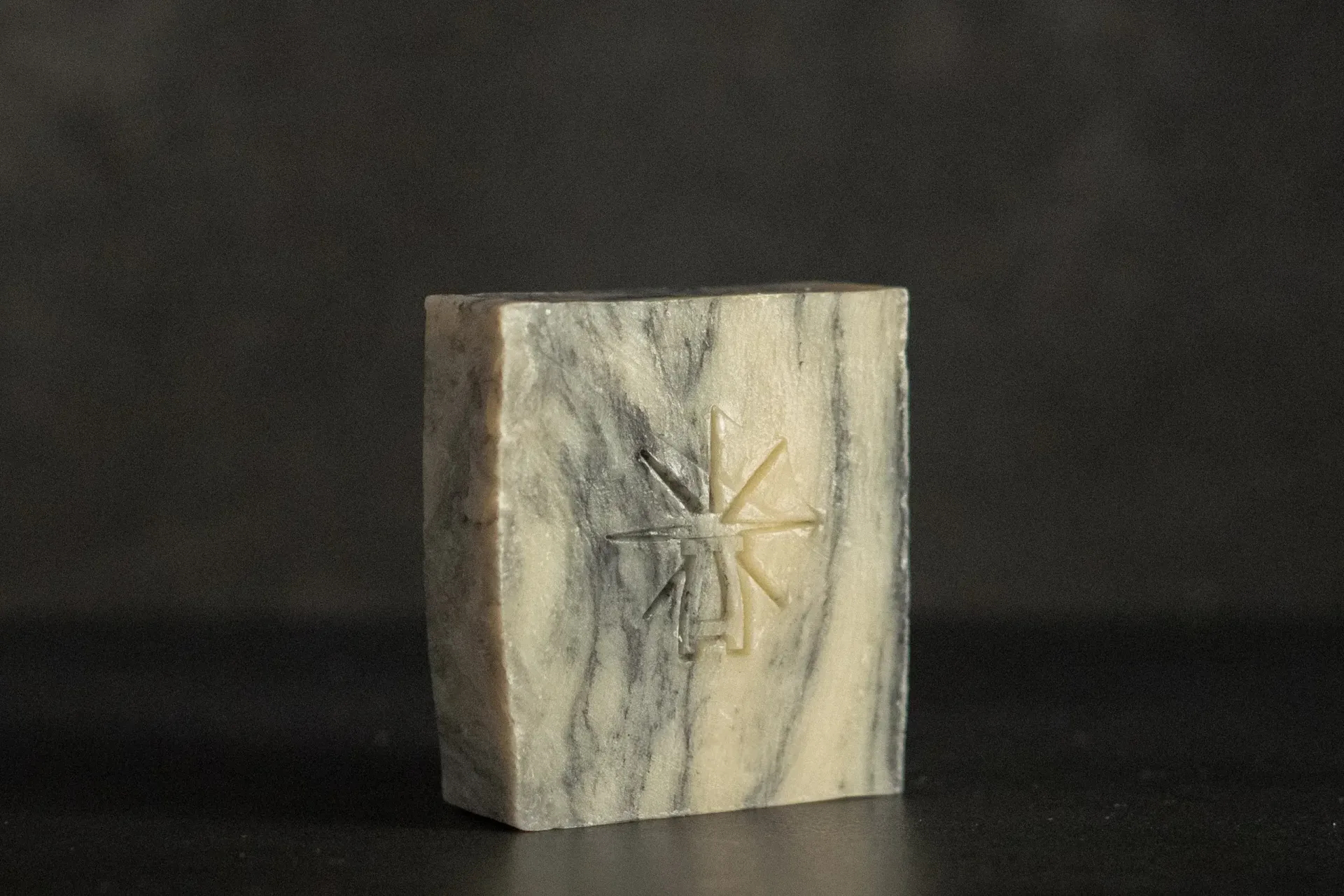 Studio shot of Black Altar Sacred Marble soap—cream and charcoal swirl bar with star-altar logo against dark background.
