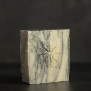 Studio shot of Black Altar Sacred Marble soap—cream and charcoal swirl bar with star-altar logo against dark background.