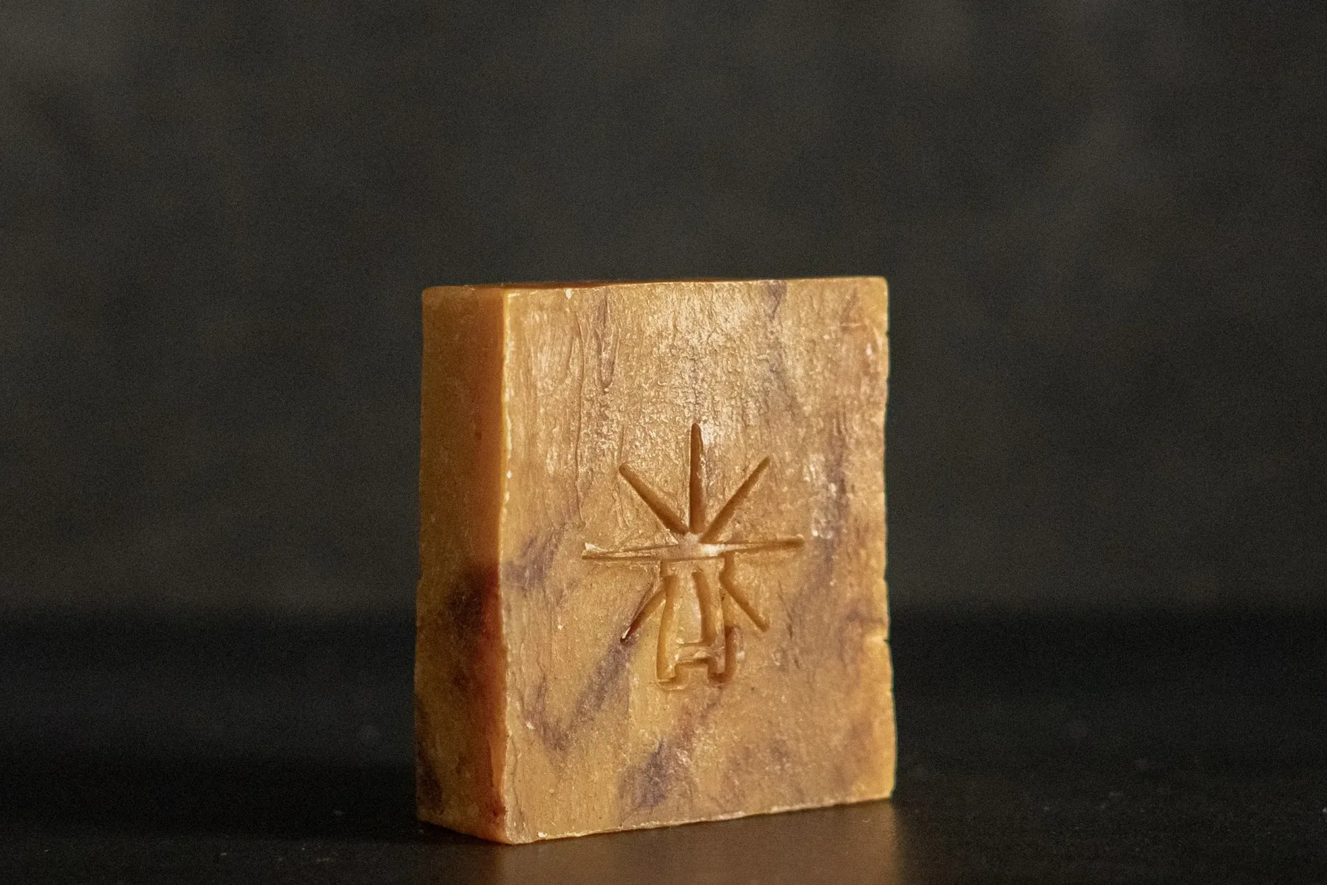 Studio shot of Black Altar Ritual Ember soap—warm amber bar marbled with deeper tones, embossed with star-altar logo.