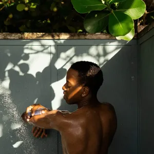 Phillip showering outdoors, sun-dappled, lathering arm with a bar of soap. twilight charcoal—lavender charcoal