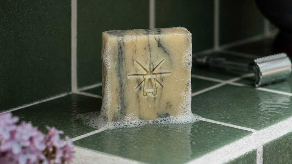 A marbled, black and white, bar sits on a green tiled shelf with suds and water around it.