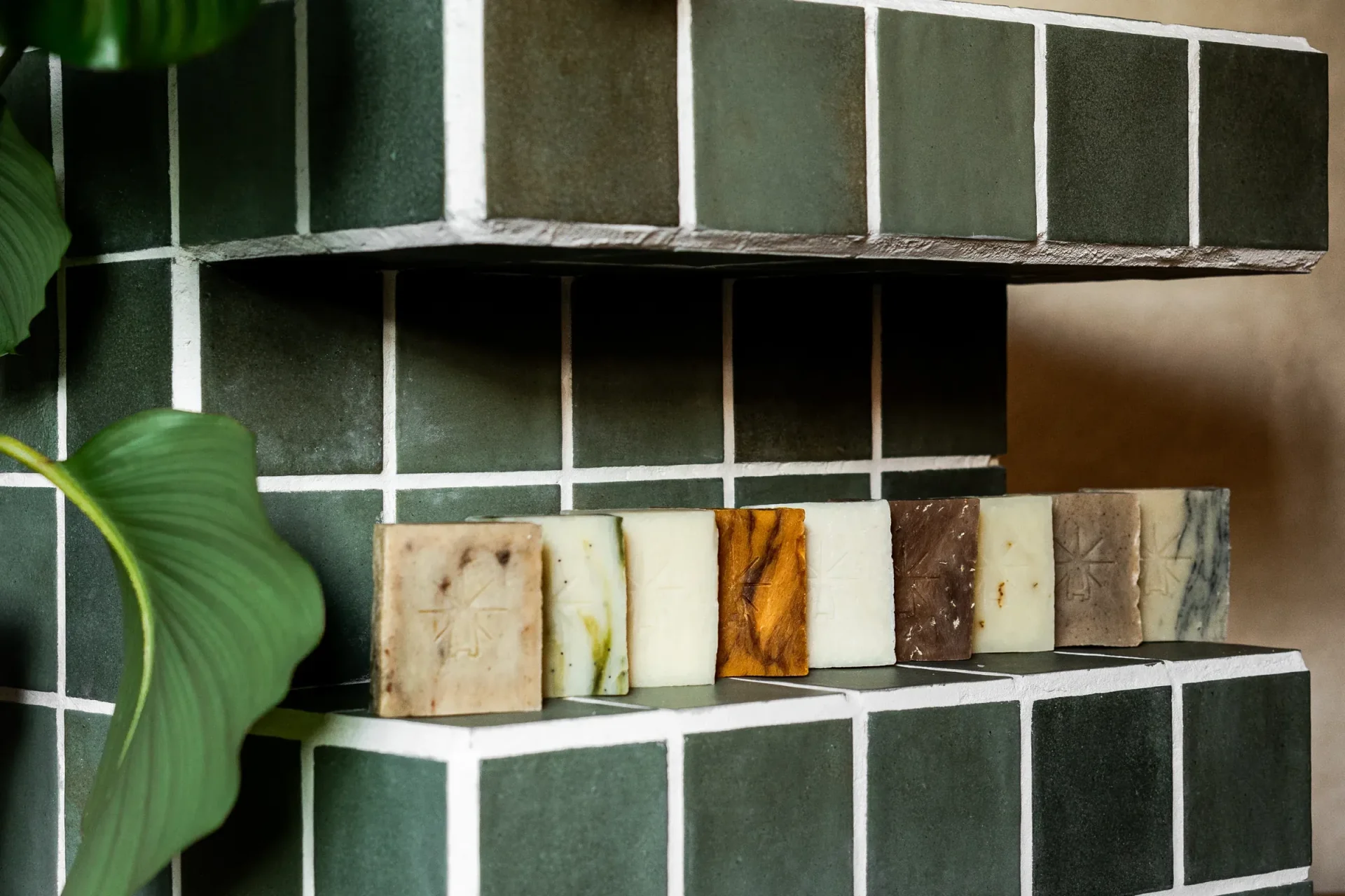 Black Altar assorted handcrafted soap bars lined on a green tiled shower shelf