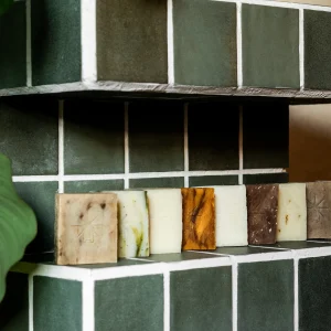 Black Altar assorted handcrafted soap bars lined on a green tiled shower shelf