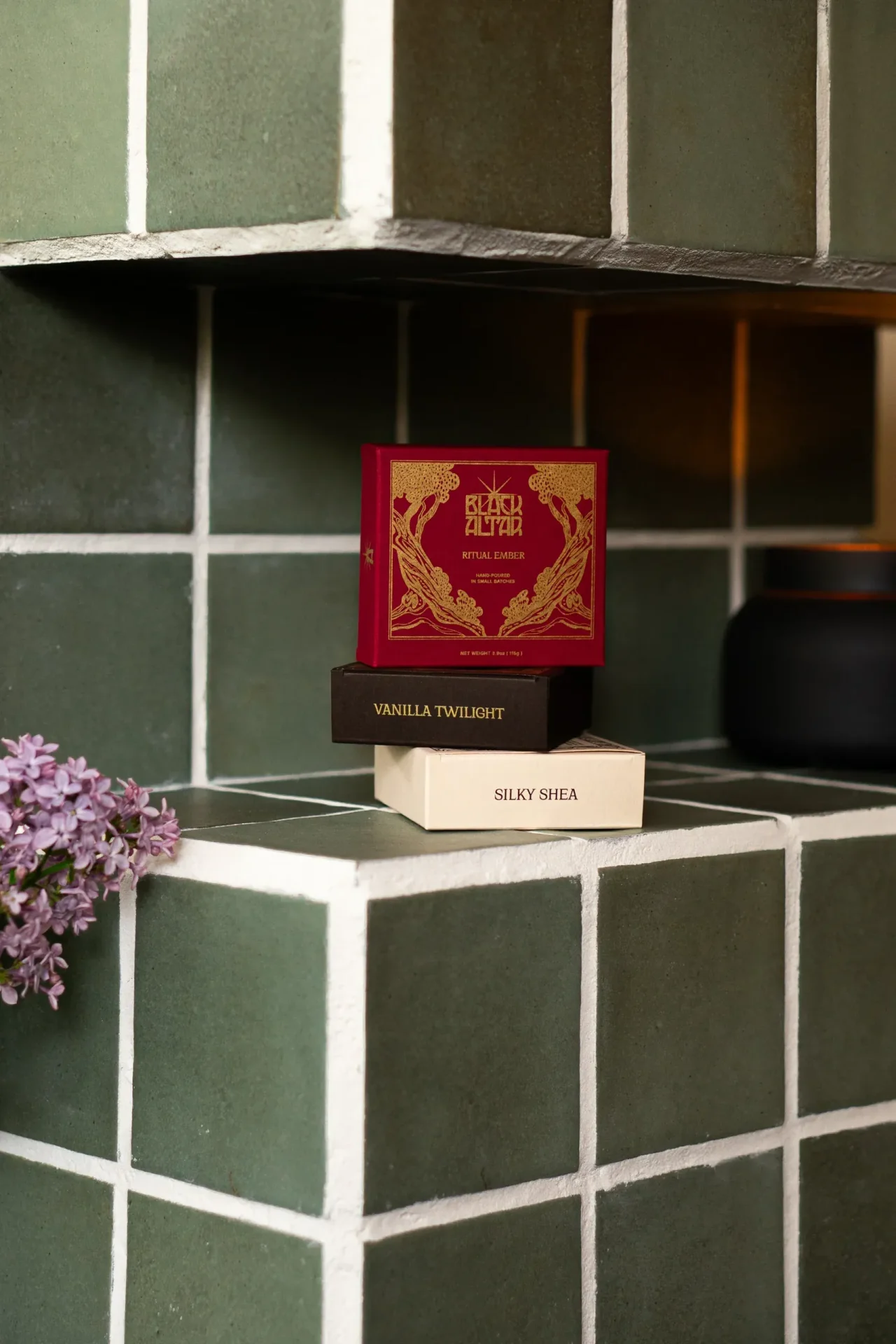 Black Altar red boxed soap propped on cream packaging beside a black candle