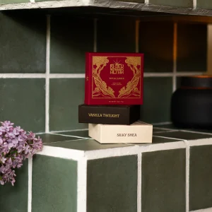 Black Altar red boxed soap propped on cream packaging beside a black candle