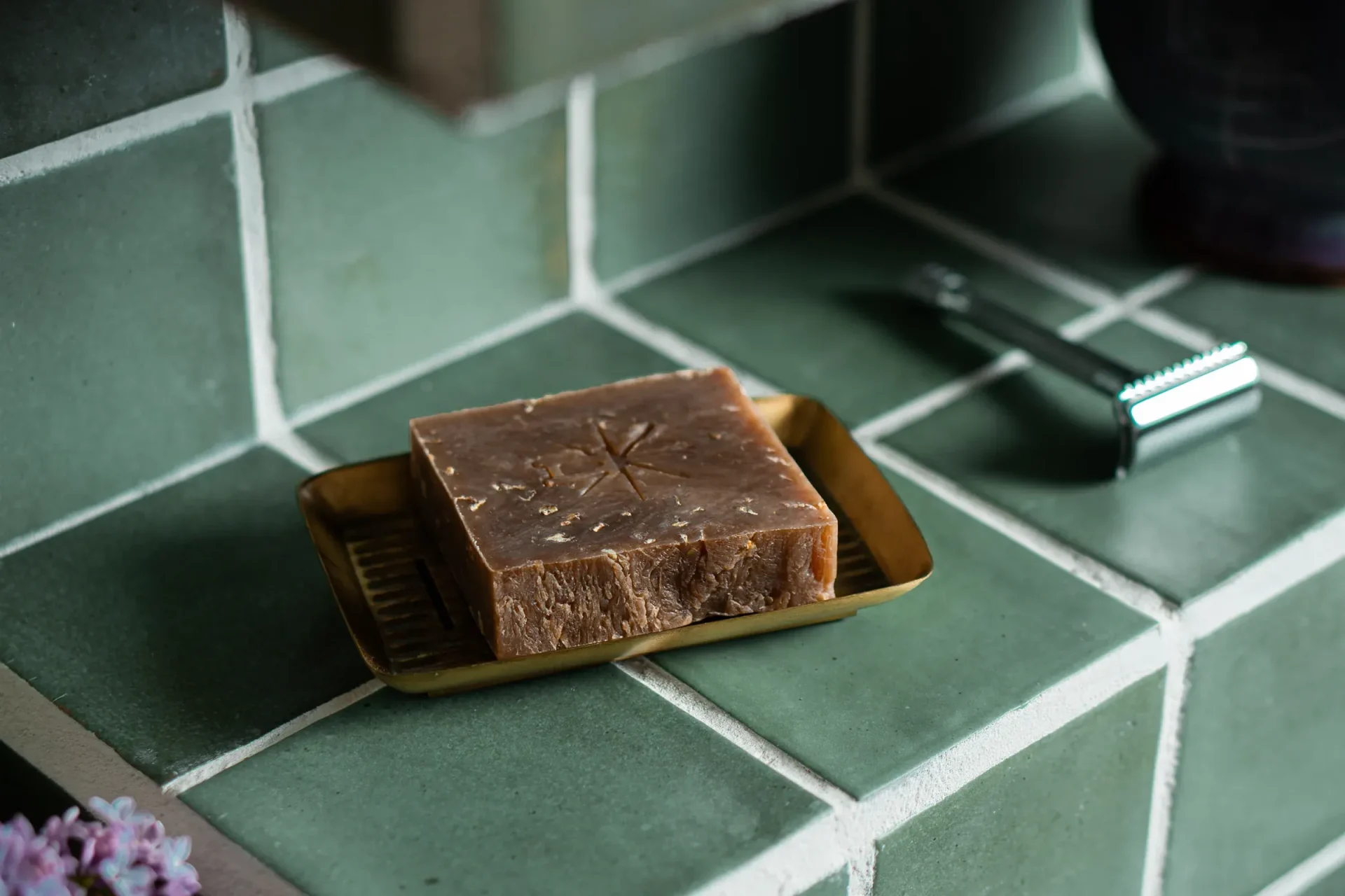 Black Altar rustic brown speckled soap bar on a brass tray against green tile