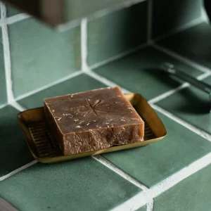 Black Altar rustic brown speckled soap bar on a brass tray against green tile