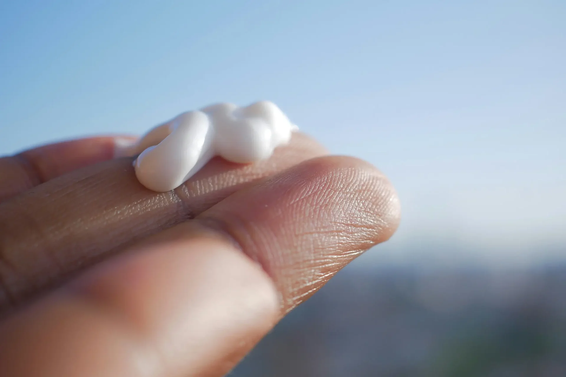 finger tips holding lotion against a blue bokeh sky